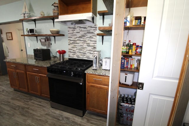 kitchen featuring dark wood-style floors, light stone counters, black range with gas stovetop, under cabinet range hood, and backsplash