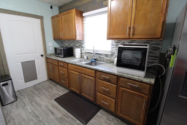 kitchen featuring light wood-style flooring, a sink, appliances with stainless steel finishes, backsplash, and brown cabinets