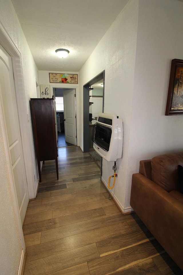 corridor featuring dark wood-style flooring, a textured wall, a textured ceiling, and heating unit