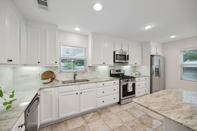 kitchen with plenty of natural light, decorative backsplash, stainless steel appliances, white cabinetry, and a sink