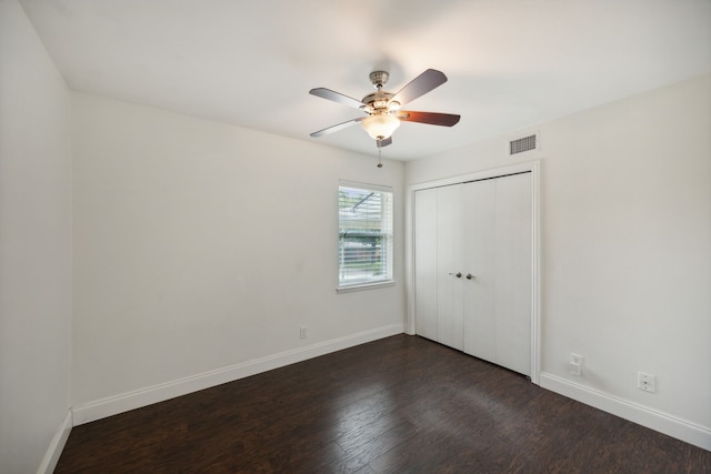 unfurnished bedroom with dark wood-style floors, visible vents, baseboards, and a closet