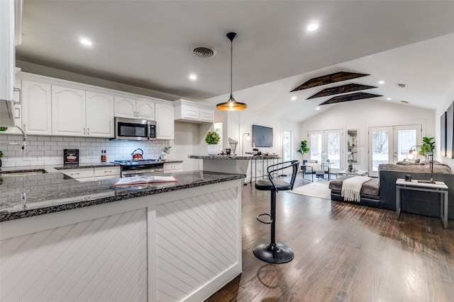 kitchen with french doors, stainless steel appliances, a sink, dark stone countertops, and a peninsula