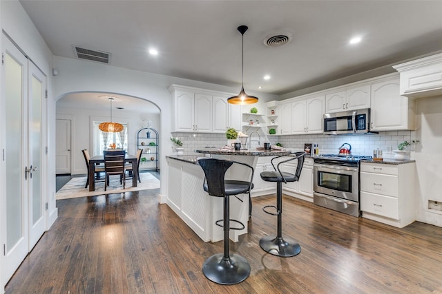 kitchen with arched walkways, white cabinetry, appliances with stainless steel finishes, open shelves, and dark wood finished floors