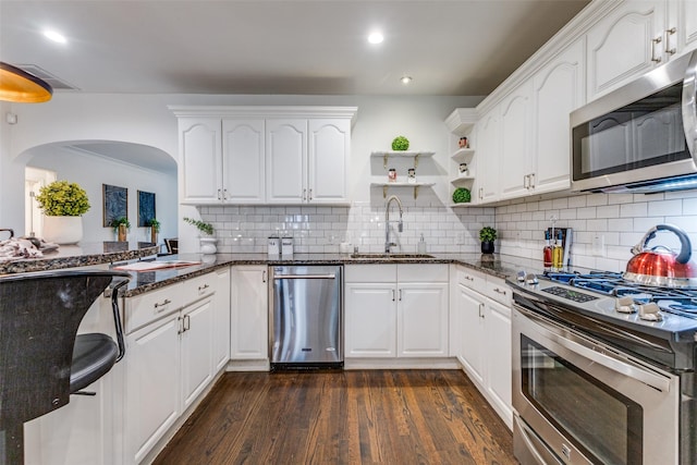 kitchen featuring dark stone counters, stainless steel appliances, a sink, and white cabinetry