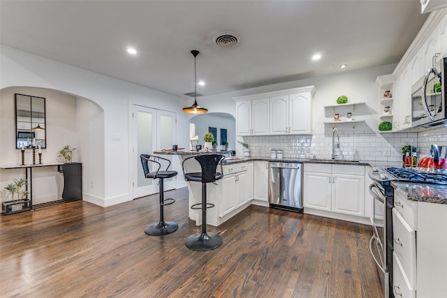 kitchen featuring arched walkways, stainless steel appliances, white cabinetry, a sink, and a peninsula