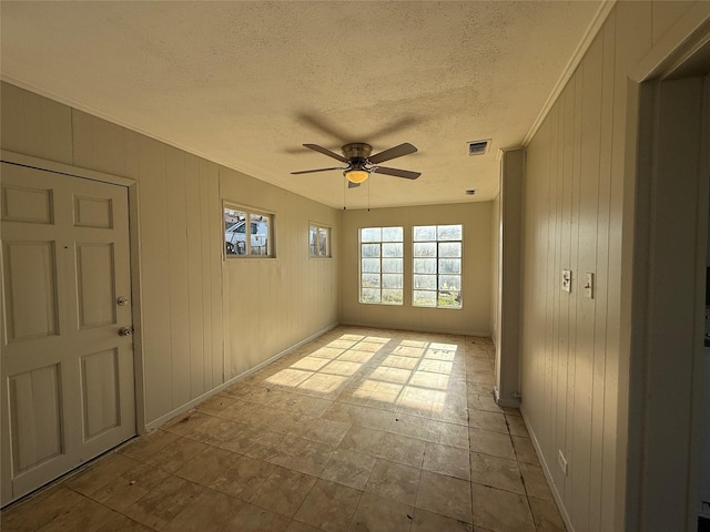 empty room featuring visible vents, ceiling fan, crown molding, a textured ceiling, and wood walls