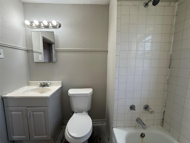 bathroom with shower / bathtub combination, a textured wall, vanity, and toilet