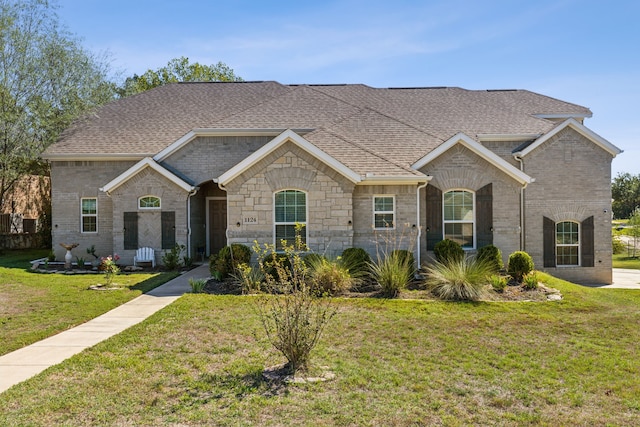 view of front of home featuring a shingled roof, a front lawn, and brick siding