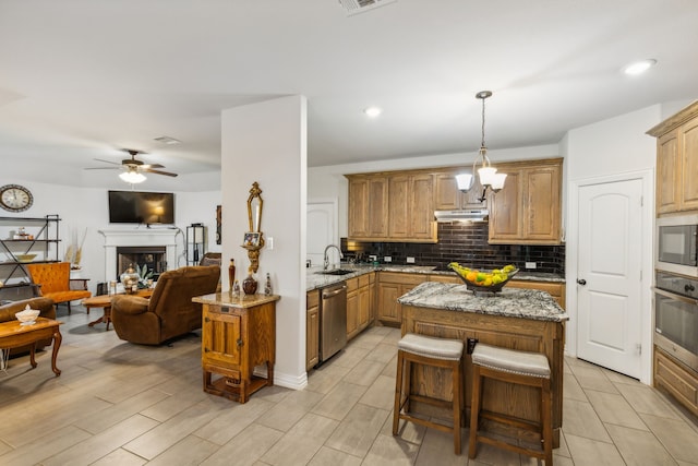 kitchen featuring a fireplace, a sink, open floor plan, appliances with stainless steel finishes, and decorative backsplash