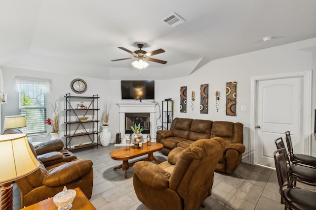 living area featuring ceiling fan, a tray ceiling, a fireplace, and visible vents