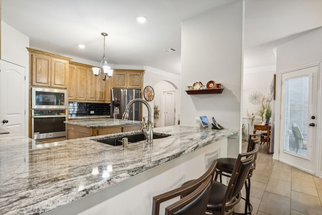 kitchen with light tile patterned floors, tasteful backsplash, appliances with stainless steel finishes, light stone countertops, and a sink