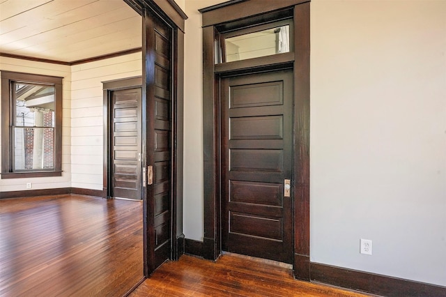 foyer entrance with dark wood finished floors, wood walls, and baseboards