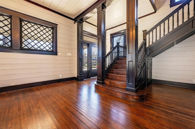 foyer with dark wood-type flooring, wood walls, baseboards, stairway, and decorative columns