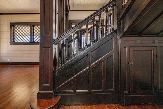 staircase featuring ornamental molding, wood finished floors, and wooden walls