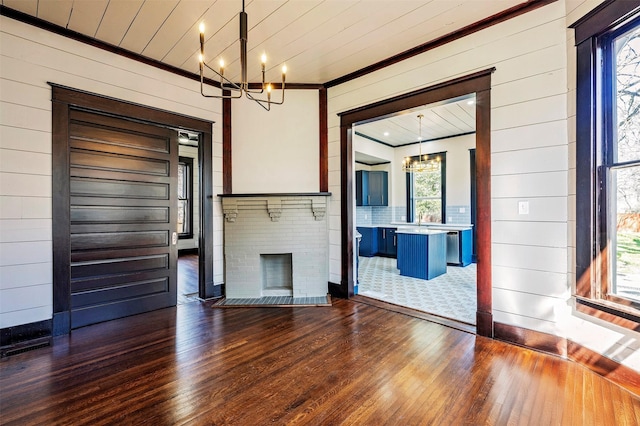 empty room with dark wood finished floors, wooden ceiling, an inviting chandelier, crown molding, and a brick fireplace