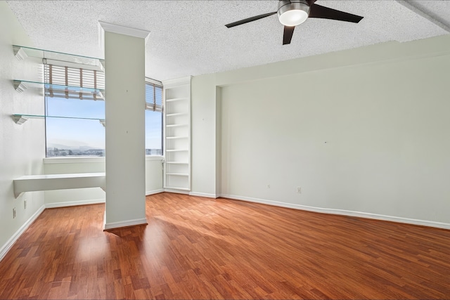 empty room featuring baseboards, a textured ceiling, a ceiling fan, built in features, and wood finished floors