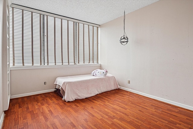 unfurnished bedroom with a textured ceiling, baseboards, and wood finished floors