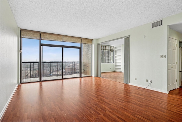 unfurnished living room with wood finished floors, a textured ceiling, baseboards, and visible vents