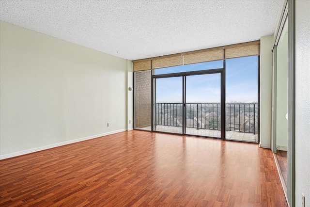 unfurnished room with a wall of windows, wood finished floors, baseboards, and a textured ceiling