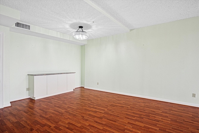 spare room with wood finished floors, a textured ceiling, baseboards, visible vents, and an inviting chandelier