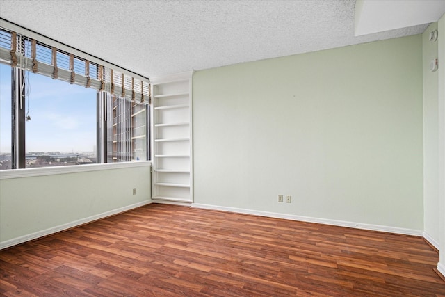 spare room with a textured ceiling, baseboards, and wood finished floors