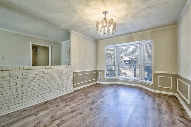 empty room with wainscoting, ornamental molding, wood finished floors, a textured ceiling, and a notable chandelier