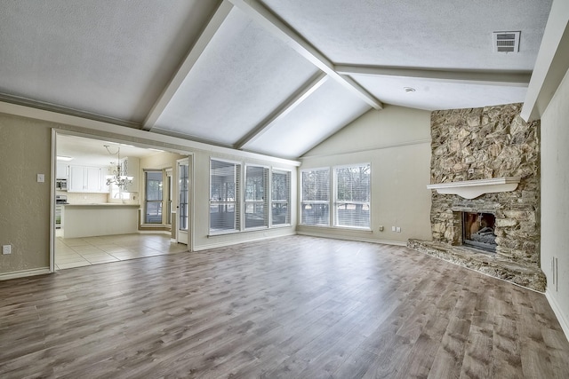 unfurnished living room featuring visible vents, a textured ceiling, a stone fireplace, light wood-type flooring, and a chandelier