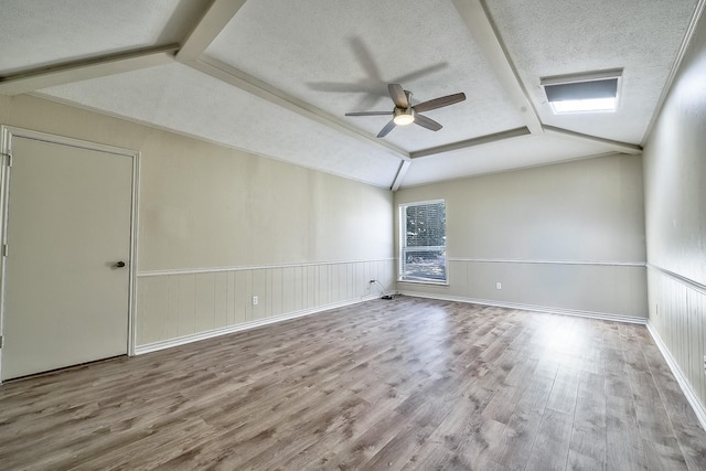 spare room featuring lofted ceiling, a wainscoted wall, light wood-type flooring, and a textured ceiling