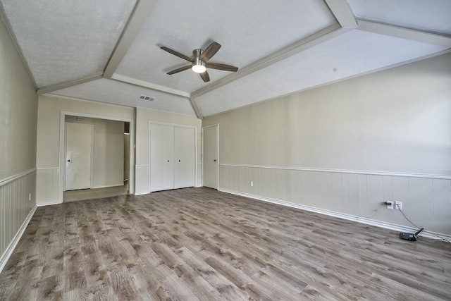 unfurnished bedroom featuring lofted ceiling, wainscoting, light wood-type flooring, and visible vents