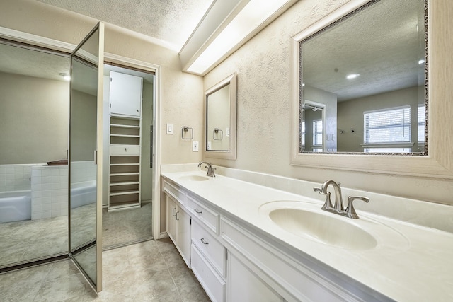 full bathroom with double vanity, a textured ceiling, a walk in closet, and a sink