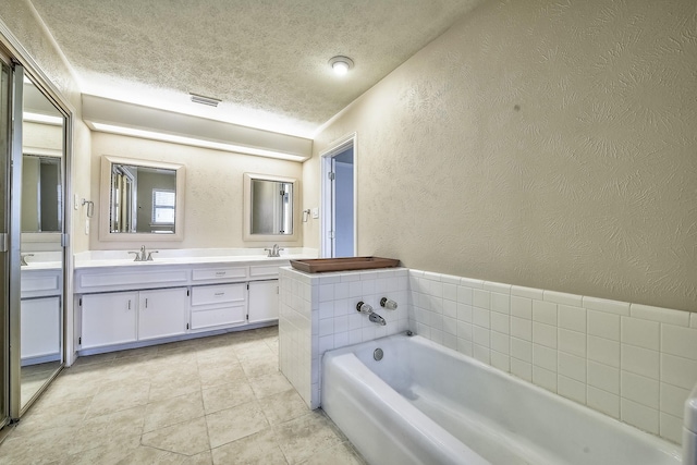 bathroom featuring a textured ceiling, a textured wall, a garden tub, a sink, and double vanity