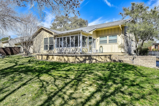 back of house featuring board and batten siding, a sunroom, fence, and a lawn