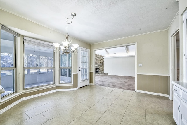 unfurnished dining area featuring a textured ceiling, light tile patterned floors, a fireplace, ornamental molding, and wainscoting