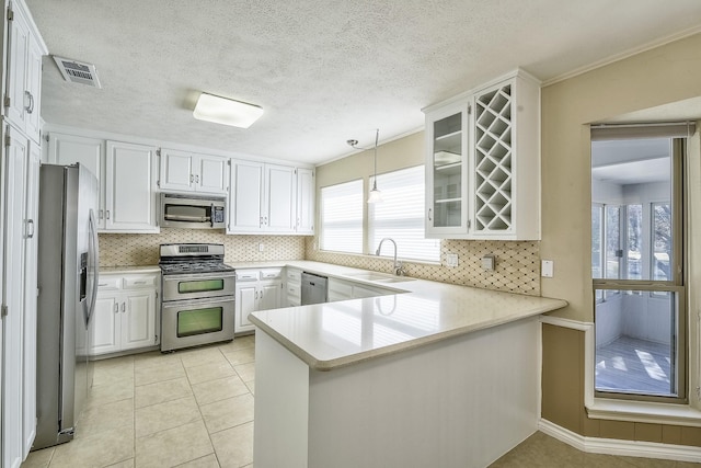 kitchen with stainless steel appliances, a peninsula, a sink, white cabinetry, and glass insert cabinets