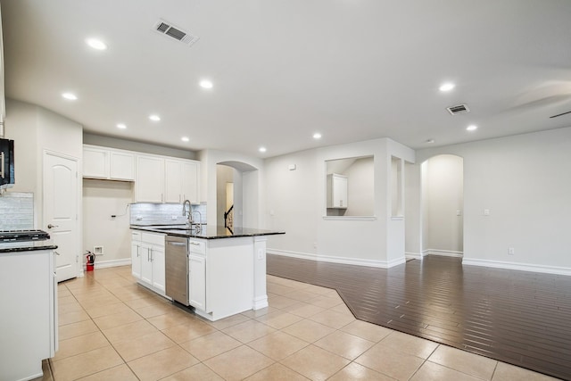 kitchen with arched walkways, stainless steel dishwasher, dark countertops, and visible vents