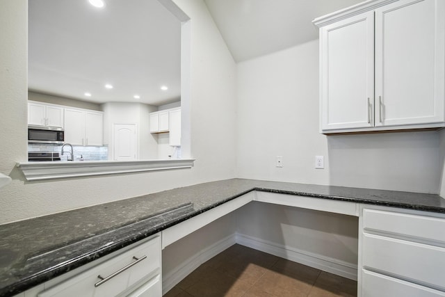 interior space with stainless steel microwave, built in desk, dark stone countertops, and dark tile patterned floors