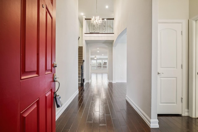 foyer featuring dark wood-type flooring, arched walkways, a notable chandelier, and baseboards