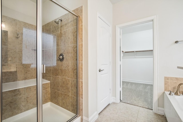 bathroom featuring baseboards, tile patterned flooring, a spacious closet, a shower stall, and a bath