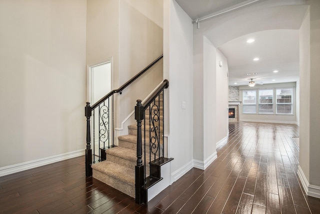 stairs featuring a large fireplace, arched walkways, wood finished floors, and baseboards