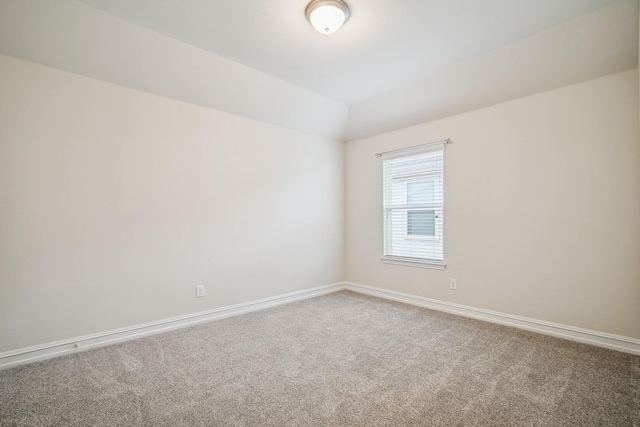 empty room featuring carpet, vaulted ceiling, and baseboards