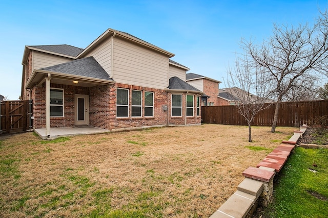 back of house with a yard, a patio, brick siding, and a fenced backyard