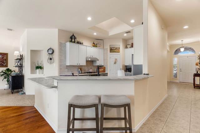 kitchen with a peninsula, under cabinet range hood, white cabinetry, and a breakfast bar