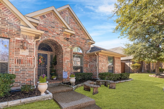 view of exterior entry with brick siding, a lawn, and fence