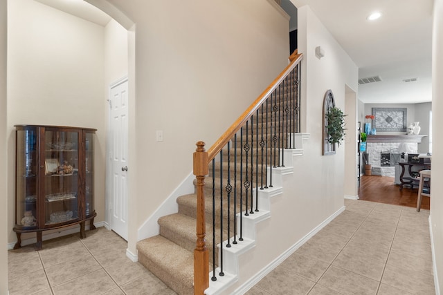 stairway featuring arched walkways, a stone fireplace, tile patterned flooring, and visible vents