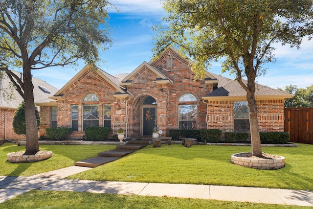 traditional home with brick siding, a front yard, fence, and a shingled roof