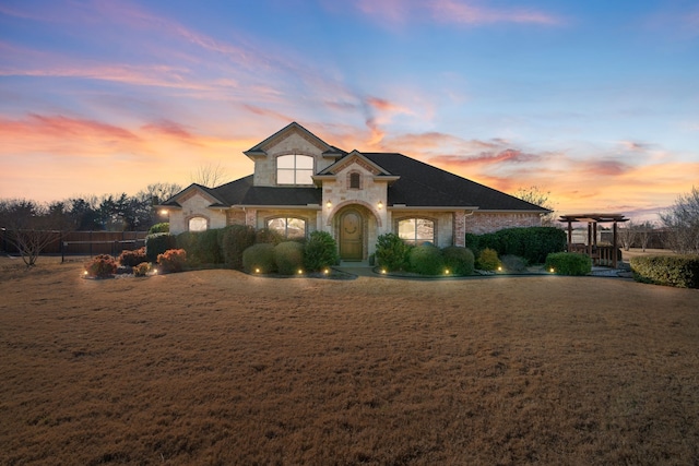 french country home with a yard, stone siding, and a pergola