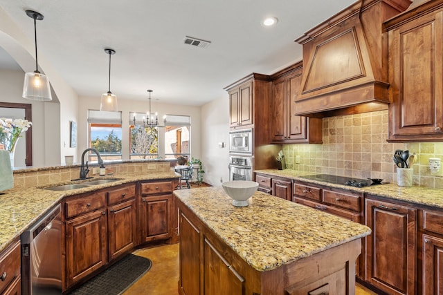 kitchen featuring decorative light fixtures, visible vents, appliances with stainless steel finishes, a sink, and premium range hood