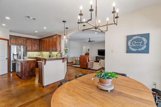 kitchen with visible vents, open floor plan, light stone countertops, stainless steel fridge, and a peninsula