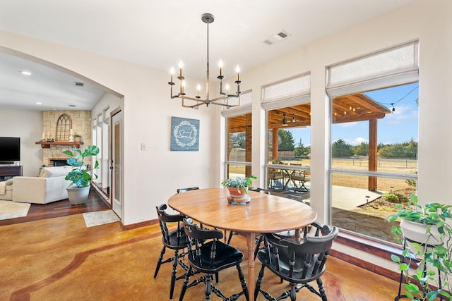 dining space with arched walkways, a stone fireplace, visible vents, baseboards, and finished concrete floors