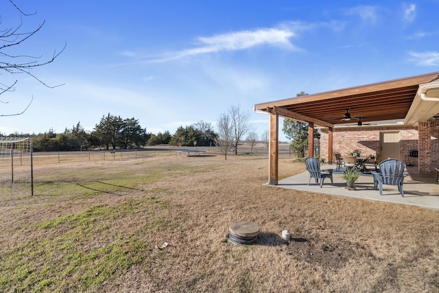 view of yard with a patio area, ceiling fan, fence, and a rural view